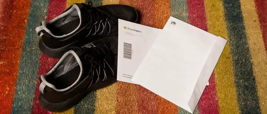 Svarta sneakers och två kuvert på färgglad randig dörrmatta